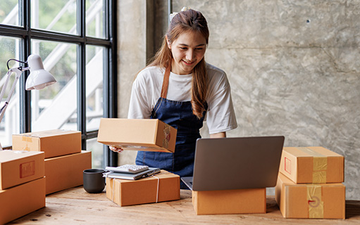 Comerciante prepara paquetes y consulta las ventas en la computadora